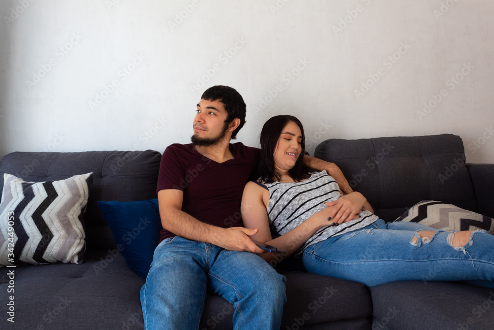 Young adult Hispanic married couple.hugging on the couch and smiling as they rest on a couch Young adult Hispanic married couple.hugging on the couch and smiling as they rest on a couch