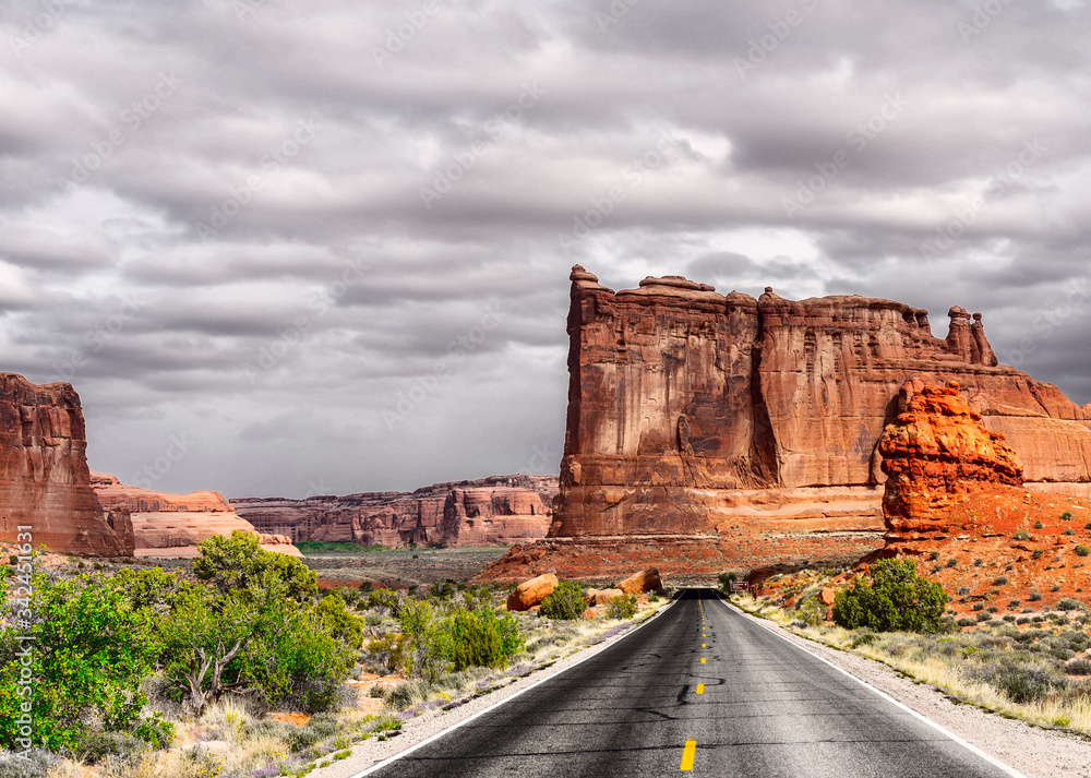 The road running through the dry prairie and rests on the red mountains on the background of a stormy sky. The road running through the dry prairie and rests on the red mountains on the background of a stormy sky.