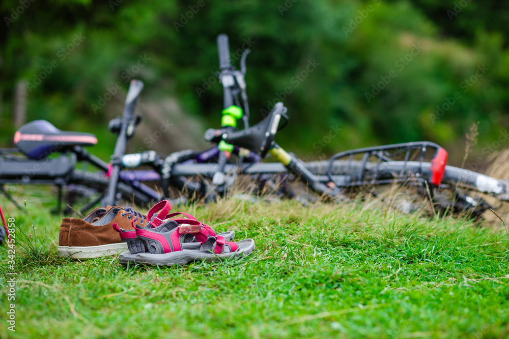 Close-up with two pairs of shoes placed on the grass in a campsite with bicycles in the background. Relaxing activity in a beautiful camping place in nature during summer.
Close-up with two pairs of shoes placed on the grass in a campsite with bicycles in the background. Relaxing activity in a beautiful camping place in nature during summer.