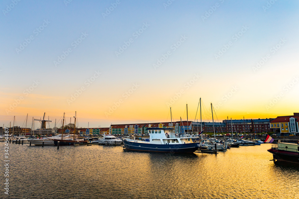 Beautiful urban sunset in a harbor in Hellevoetsluis in the Netherlands. Boats, ships and yachts docked , old wind mill and colourful buildings