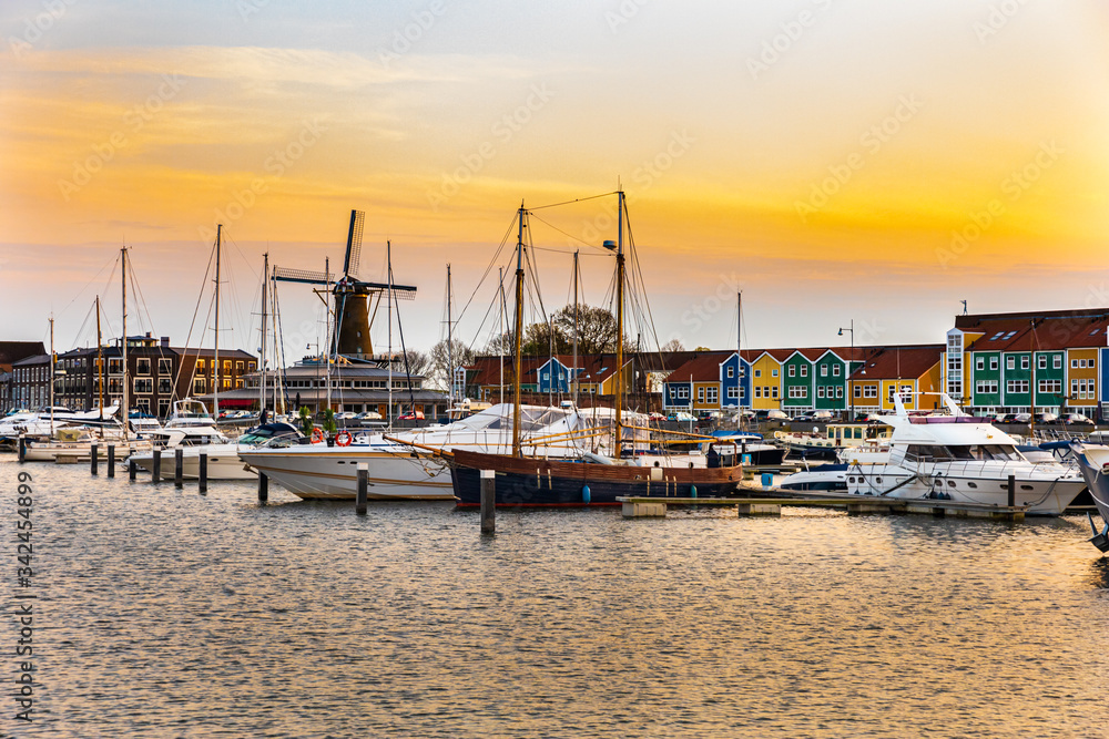Fototapeta premium Beautiful urban sunset in a harbor in Hellevoetsluis in the Netherlands. Boats, ships and yachts docked , old wind mill and colourful buildings