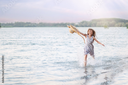 A happy young girl runs along the shore on the water and waves her hat. The girl is happy with the onset of summer