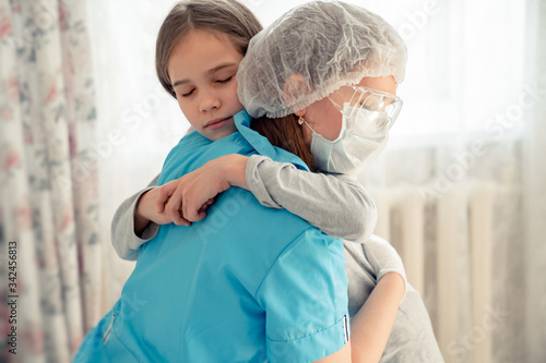 mom Doctor in mask examines kid at home and hugs.