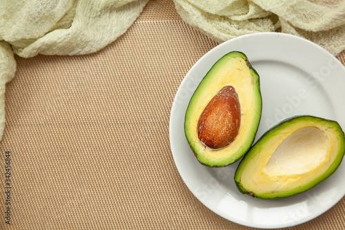 Two halves of ripe avocado on white plate and a wooden background.
