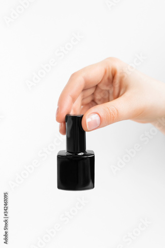 Woman holds a bottle of maroon nail polish. Grey background.