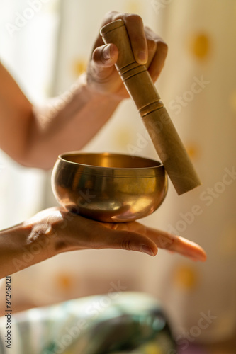 Close-up of of a young yogin woman holding a tibetan bowl and a stick in the beautiful and gentle light of morning during a yoga session, creating a meditative state through music.