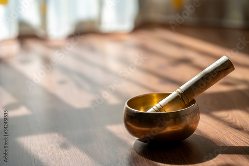 Tibetan golden bowl with a wooden stick sitting on the floor in the soft light of morning. Peaceful meditation music for mind and positive energy through healing sounds.