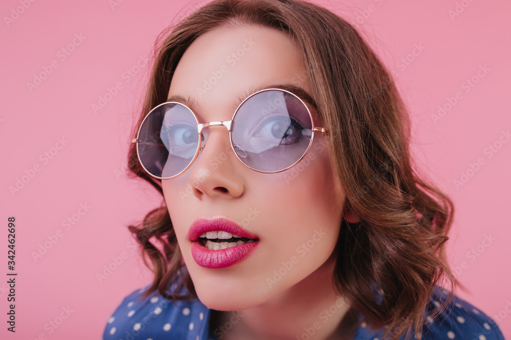 Close-up portrait of lady with pink lips posing with mouth open. Indoor photo of stunning european female model in sunglasses isolated on pastel background. Close-up portrait of lady with pink lips posing with mouth open. Indoor photo of stunning european female model in sunglasses isolated on pastel background.