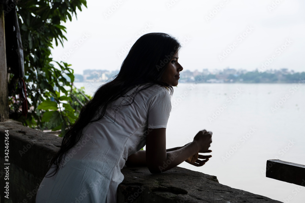 Portrait of a beautiful dark skinned brunette Indian lady in white ethnic dress standing in front of a lake in a sunny morning. Indian lifestyle. Portrait of a beautiful dark skinned brunette Indian lady in white ethnic dress standing in front of a lake in a sunny morning. Indian lifestyle.