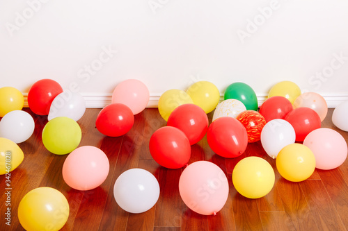 Group of many colorful air balloons lying on floor in studio apartment. Decoration interior for a birthday holiday celebration. Festive background with copyspace.