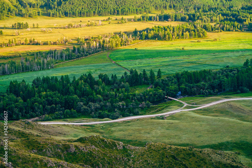 Aerial scenic view to agricultural field in sunlight. Vivid landscape of countryside with field, forest, mountain river, bridge, dirt road and fence at sunset. Beautiful country land in evening light.