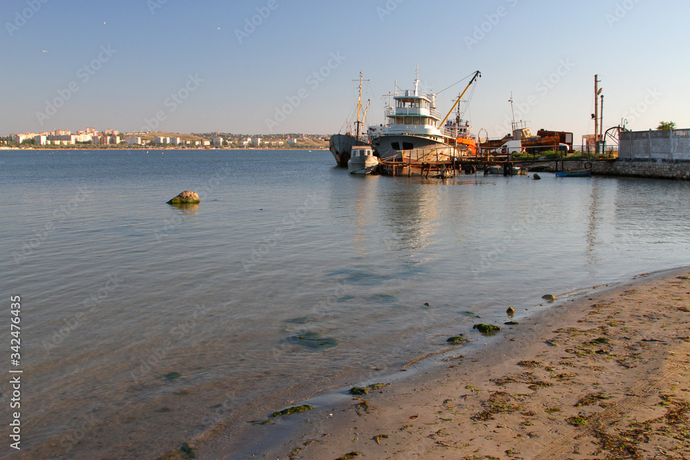 Fototapeta premium Beach and seashore with a pier and fishing boats in the background. Sea resort town in the background