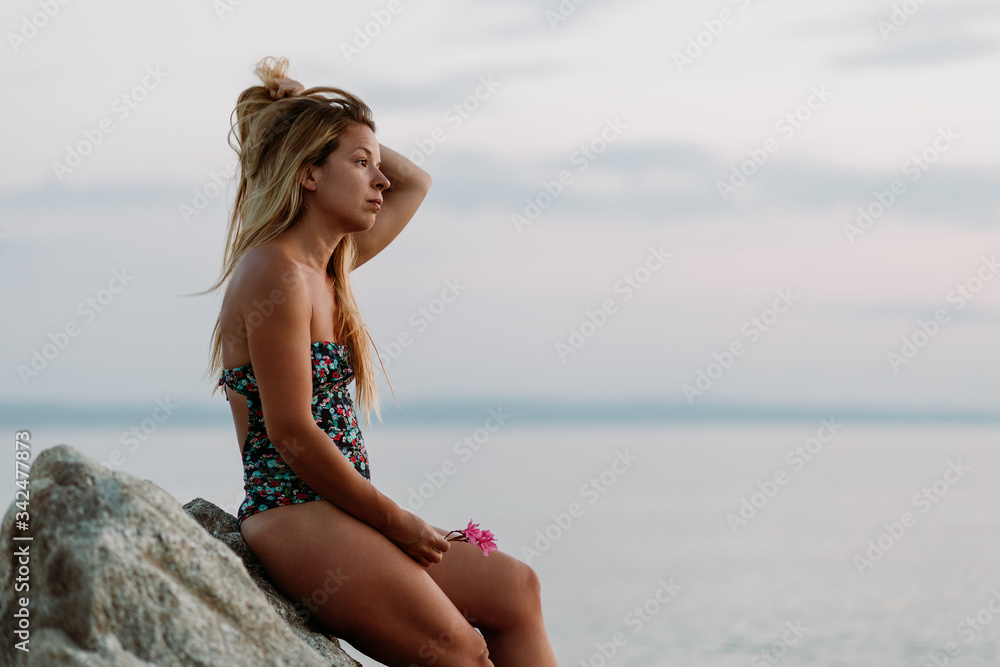 Young beautiful woman sitting on the rock by the sea