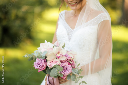summer tender portrait of a bride with a bouquet on a park background, focus on a bouquet, cropping on the nose 