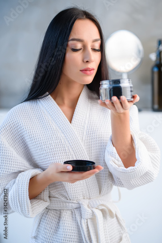 A girl in a white gown holds a hair care product in the bathroom and feels the flavor. A beautiful bottle in the hands of a girl. means of hygiene