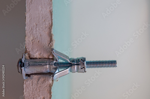 Metal Molly fastener fixed in a pre-drilled hole in a sheet of moisture-resistant drywall, split view.  The sheet is cut at the installation site, showing the gypsum fiber and connection details.