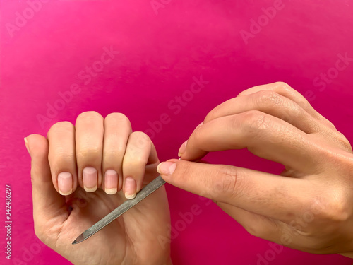 Woman s girl s hand filing nails with metal nail file on a pink background. Self manicure