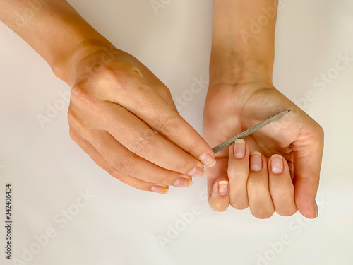 Woman's girl's hand filing nails with metal nail file on a white background. Self manicure
