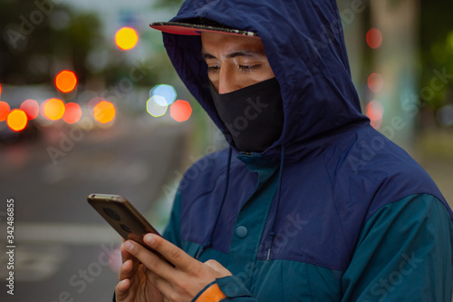 A man uses a face mask and looks his smartphone on the street