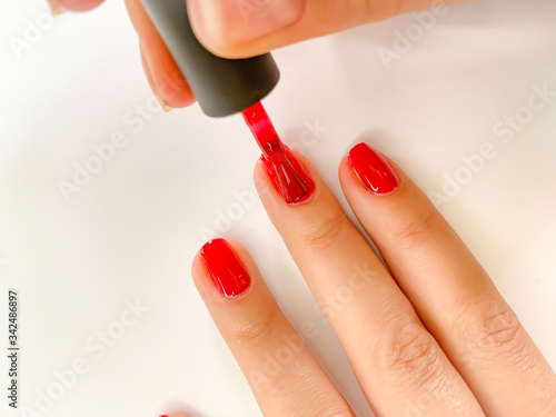 Female woman painting her nails in red color on a white background