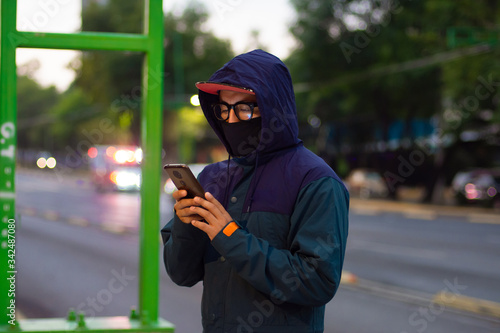 A man wearing a face mask and a hood using his smartphone on the street