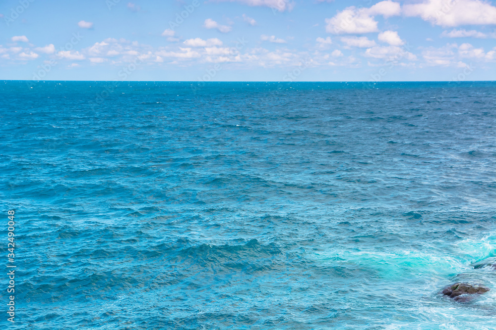 Fototapeta premium rocky sea shore in the afternoon. blue waves crashing the coast. fluffy clouds above the horizon.