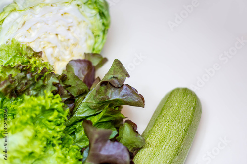 Still life of fresh, green vegetables. Zucchini, young cabbage, lettuce. On a gray background. It is located on the left. Space for text. Vertical photo. The view from the top