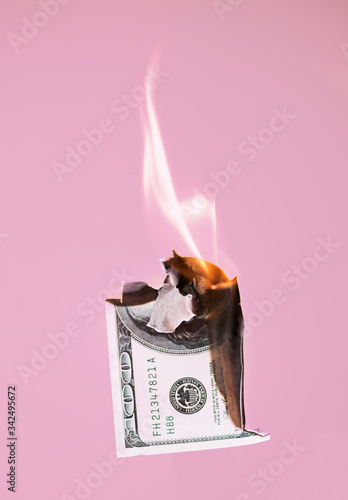 Burning hundred dollars cash on pink background
