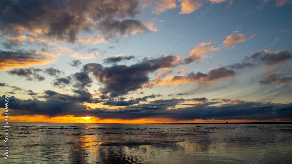 Fototapeta premium Beautiful clouds in the sunset rays on the sandy beach of the sea.