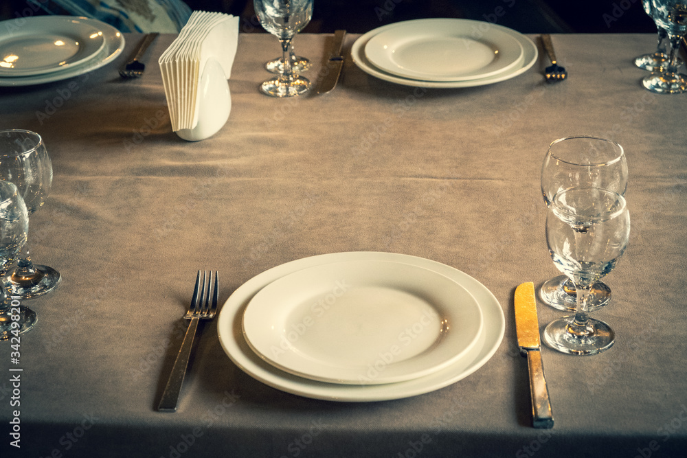 The served table in the restaurant. Clean dishes and appliances on the tablecloth in a cafe. Shiny transparent glasses. White plates. Prepared for the reception of guests. High service. The served table in the restaurant. Clean dishes and appliances on the tablecloth in a cafe. Shiny transparent glasses. White plates. Prepared for the reception of guests. High service.