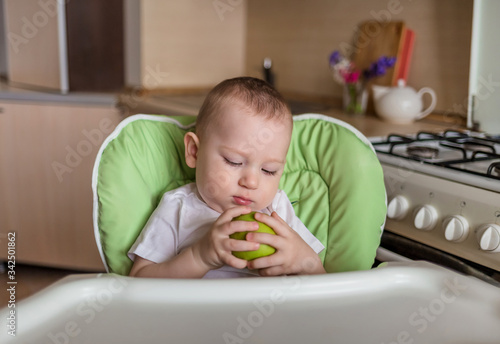 Baby boy sits in a chair and eats green apple. Baby boy eats proper nutrition. Ecological products