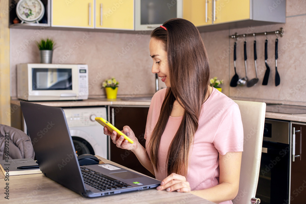 Distance learning online-education and work.Girl working in an office remotely from home in the kitchen. Use the computer and drink coffee. She communicates with friends and family on the phone Distance learning online-education and work.Girl working in an office remotely from home in the kitchen. Use the computer and drink coffee. She communicates with friends and family on the phone