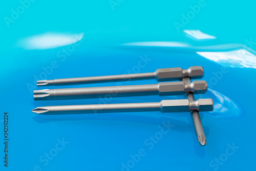 Fototapeta Naklejka Na Ścianę i Meble -  Three parallel arranged screwdriver bits for slotted-head and cross-head screws and positioned in a right angle to one cross-head screwdriver bit on turquoise background