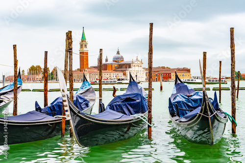 Venice, Italy. Empty Gondolas/ Gondole docked by lagoon mooring poles. Famous romantic city tour boat ride for tourists/ couples/ people. Bell Tower San Giorgio Maggiore Basilica Church in background © Debbie Ann Powell