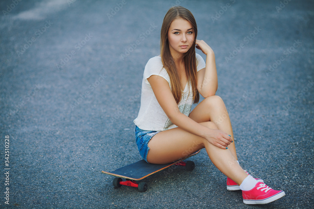 A young girl in short shorts sitting on a skateboard. Stock Photo