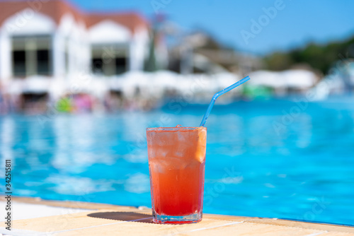 Fresh alcoholic red cocktail sex on beach with ice in glass on edge of pool in summer weather against background washed up pool and recreation area. Concept good holiday and travel  place for text.