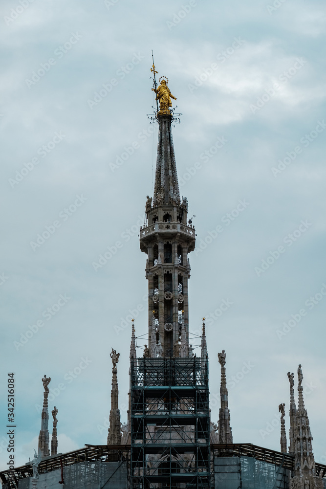 Obraz premium Pinnacle with the golden sculpture of Madonnina, Santa Maria, on top of the roof of Milan Cathedral