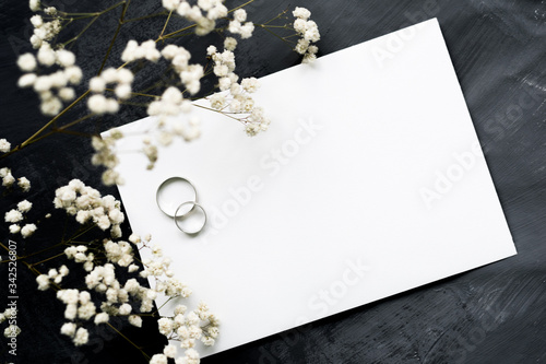 Gypsophila branches and white gold wedding rings for a card or wedding invitation. White sheet of paper for inscription on a gray background, copyspace