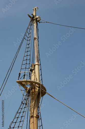 View of an old tall ship mast with rigging and shrouds against a deep blue sky, vertical aspect