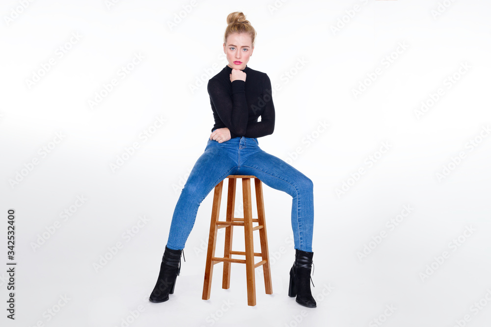 Sexy girl in tight jeans sitting on stool with legs apart and chin resting  on fist. Stock Photo | Adobe Stock