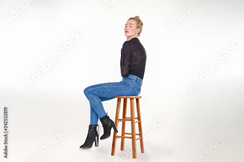 Pretty teen girl in skinny jeans and black sweater seated  on wooden stool.
