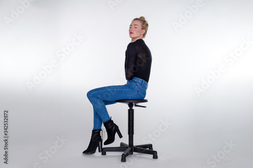 Pretty teen girl in skinny jeans seated on modern stool.
