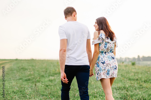 Young couple in love walking on through grass field. Walking along grass field.