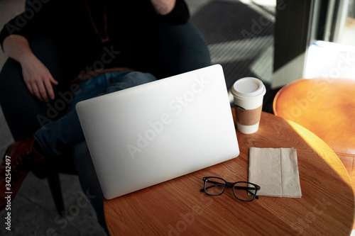 Man working with computer at a coffee shop with cup and glasses on the table