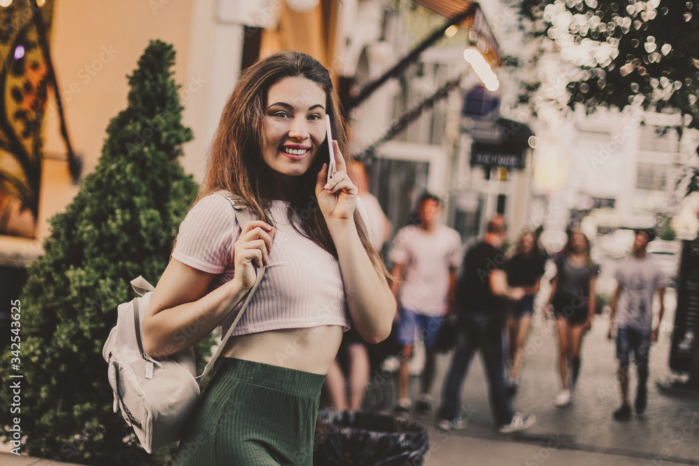 Smiling woman using phone and drink coffee on the street in summer day.