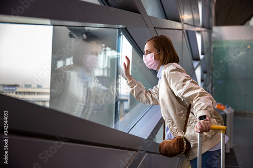 Sad woman passenger wearing medical face mask, looking at window at almost empty airport terminal due to coronavirus pandemic, Covid-19 outbreak travel restrictions. Flight cancellation.