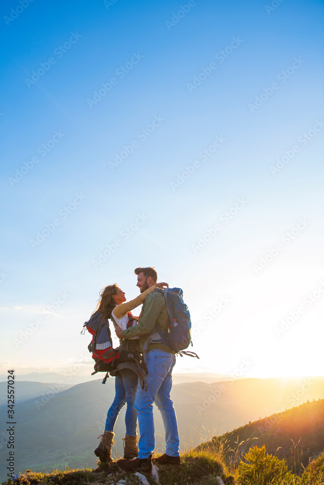 Hikers with backpacks relaxing on top of a mountain and enjoying the view of valley Hikers with backpacks relaxing on top of a mountain and enjoying the view of valley