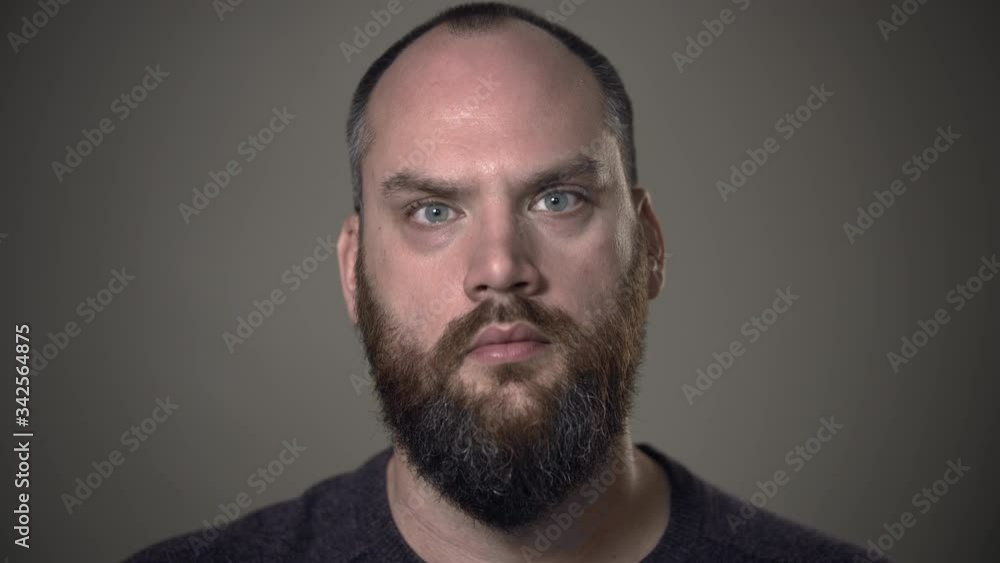Bearded man in his 30s stares with no expression into camera. Somber theme of pain, sorrow, sadness, depression. Bearded man in his 30s stares with no expression into camera. Somber theme of pain, sorrow, sadness, depression.