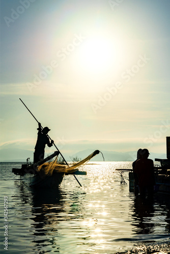 Lake and Silhouette of Asian fisherman on boat casting a net for catching freshwater fish in nature river in the early morning at Dau Tieng lake, Tay Ninh, Vietnam  photo