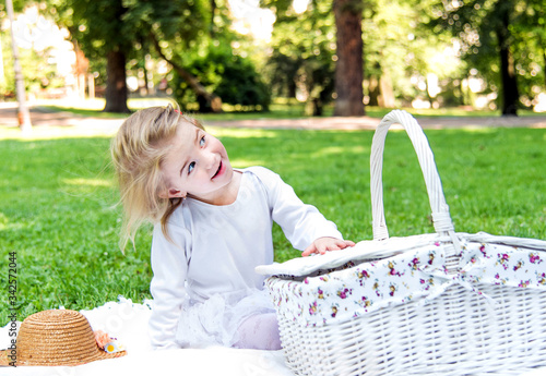 A little beautiful girl walks in the park with a picnic basket and straw hat. Funny emotional baby.